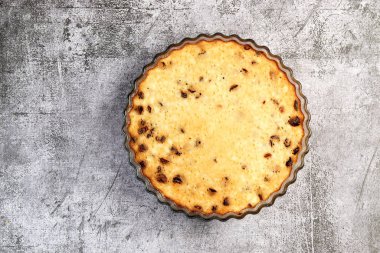 Koyu gri arka planda, cam bir kabın içinde kurutulmuş yaban mersinli süzme peynir güveci. Üst manzara, düz uzanma