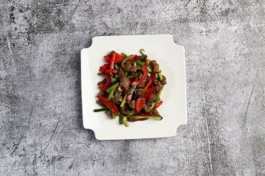 Cucumber and beef salad with bell pepper on a white square  plate on a dark background. Top view, flat lay