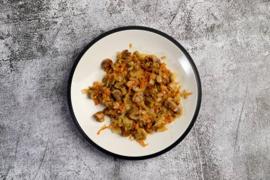 Stewed cabbage with champignon mushrooms on a round plate on a dark gray background. Top view, flat lay