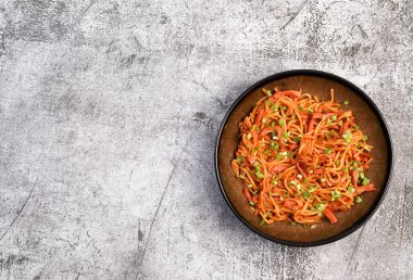 Koyu gri arka planda yuvarlak tabakta yeşil soğanlı baharatlı sosisli şehriye. Üst manzara, düz uzanma