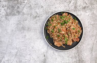 Koyu gri arka planda yuvarlak tabakta eti olan karabuğday pilavı. Üst manzara, düz uzanma