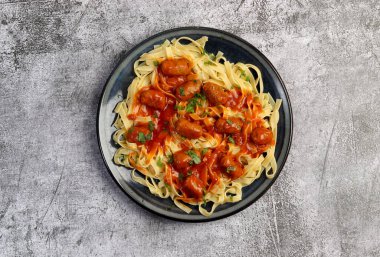 Koyu gri arka planda yuvarlak tabakta sosis ve domates soslu Tagliatelle makarnası. Üst manzara, düz uzanma