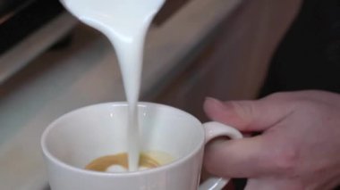 Kahveci bir cappuccino yaptı. Köpüğe kalp çizerek espresso ile çırpılmış sütü bardağa doldurur.