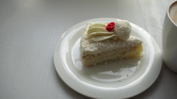 左側の白いプレートの上に 白いケーキの一部です それは 上の白いクリームとラファエロキャンディーに ココナッツのシェービングが振りかけられています 一晩で心臓のパターンを持つ白血球減少症です — ストック動画