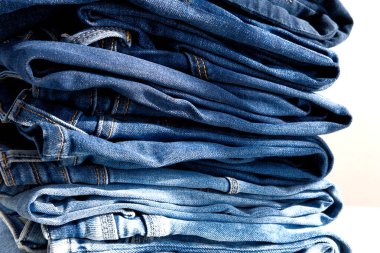 Beyaz arka planda bir yığın kot pantolon. Güneş ışığı. Kapat.