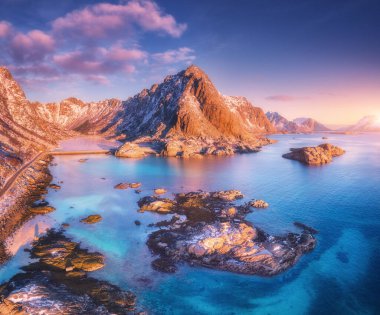 Güzel dağların havadan görünüşü, denizdeki küçük adalar, yol, gün batımında mavi gökyüzü Lofoten adalarında, kışın Norveç. Yol manzarası, karlı kayalar, taşlar, deniz kıyıları, temiz su. Üst görünüm