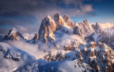 Kışın gün batımında kar altında güzel dağ zirveleri. Yüksek sisli karlı kayalarla dolu renkli bir manzara, soğuk akşamlarda bulutlu mavi bir gökyüzü. Dolomites, İtalya 'da Tre Cime. Alp dağları. Doğa