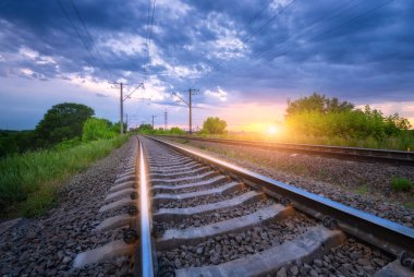 Yazın altın gün batımında demiryolu ve güzel mavi gökyüzü. Tren istasyonu ve bulutlu gökyüzü. Demiryolu platformu, yeşil ağaçlar ve çimenler ile endüstriyel manzara, akşamları dramatik bulutlu gökyüzü