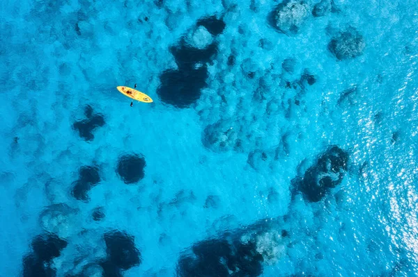 夏の日没で青い海の黄色のカヤックの空中ビュー 澄んだ紺碧の水の中に浮かぶカヌーの上の男 ギリシャのレフカダ島 熱帯の風景 ボードだ アクティブな旅行 最上階だ — ストック写真