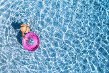 Şapkalı genç bir kadının mavi denizde pembe yüzme yüzüğüyle yüzüşünü yazın günbatımında balık sürüsüyle görüntüsü. Kızlı tropik manzara, temiz su, Yunanistan 'da kumlu plaj. Üst Manzara. Seyahat