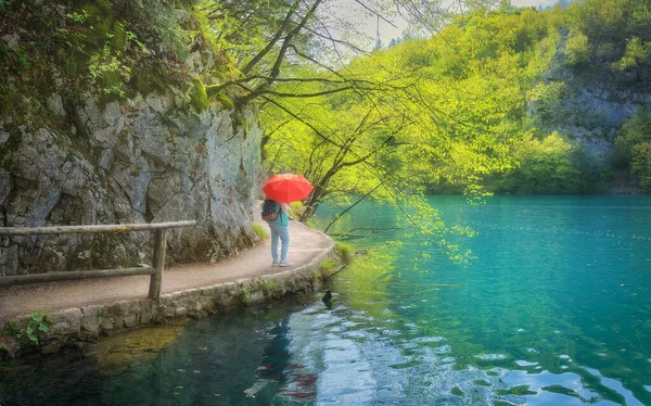 Žena s červeným deštníkem na cestě poblíž krásného jezera v dešti — Stock fotografie