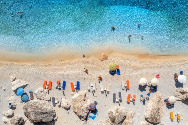 Mavi deniz manzarası, şemsiyeli kumlu sahil, taşlar ve kayalar, yazın günbatımında berrak su. Lefkada Adası, Yunanistan. Deniz kıyıları, yüzen insanlar, mavi sular olan tropik bir manzara. Üst görünüm