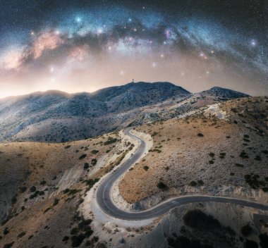 Samanyolu kemeri ve dolambaçlı dağ yolu geceleri. Kemerli samanyolu gökyüzü ve yazın parlak yıldızlar. Lefkada, Yunanistan. Boş yol manzarası, tepeler. Otoyolu ve uzayı olan güzel bir manzara. Seyahat