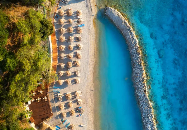 Aerial view of sandy beach with umbrellas, sea, green trees, breakwater at sunset in summer. Blue lagoon in Oludeniz, Turkey. Tropical landscape with sea bay, transparent water. Top view from drone