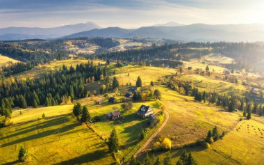 Ukrayna 'da sonbaharda günbatımında Carpathian dağlarındaki güzel köyün hava manzarası. Yeşil çayırlar, evler, bahçeler, ağaçlar, sonbaharda gökyüzü olan renkli bir manzara. Dağ kırsalının en üst manzarası