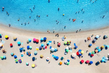 Aerial view of colorful umbrellas on sandy beach, people in blue sea at sunset in summer. Tuerredda Beach, Sardinia, Italy. Tropical landscape with turquoise water. Travel and vacation. Top view clipart