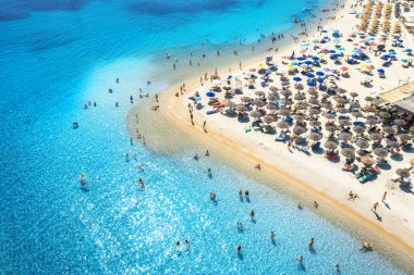 Aerial view of colorful umbrellas on sandy beach, people in blue sea at sunset in summer. Tuerredda Beach, Sardinia, Italy. Tropical landscape with turquoise water. Travel and vacation. Top view
