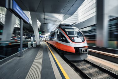 High speed train in motion inside modern train station in Vienna. Fast red intercity passenger train with motion blur effect. Railway platform. Railroad in Europe. Commercial transportation. Concept