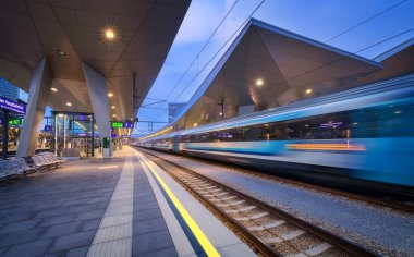 High speed train in motion on the railway station at night. Moving blue modern intercity passenger train, railway platform, architecture, city lights. Modern train station in Vienna, Austria. Railroad