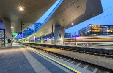 High speed train in motion on the railway station at night. Moving red modern intercity passenger train, railway platform, architecture, city lights. Modern train station in Vienna, Austria. Railroad
