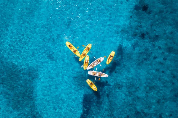 Aerial view of yellow kayaks in blue sea at sunset in summer. People on floating canoes in clear azure water. Sardinia island, Italy. Tropical landscape. Sup boards. Active travel. Top view from drone