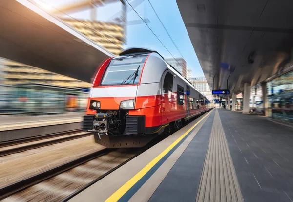 High speed train in motion on the train station at sunset in Vienna. Red modern intercity passenger train with motion blur effect. Railway platform. Railroad in Europe. Commercial transportation