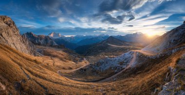 Beautiful view on mountains at sunset in autumn. Nature in Dolomites, Italy. Colorful panoramic landscape with rocks, orange grass in hills, trail, dirt road, stones, blue sky with clouds in fall