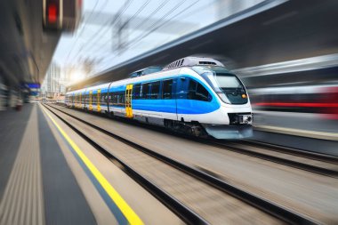 Yüksek hızlı tren gün batımında tren istasyonunda hareket halinde. Hareket bulanıklığı olan mavi modern şehirlerarası yolcu treni. Demiryolu platformu. Avrupa 'da demiryolu. Ticari ulaşım. Kavram