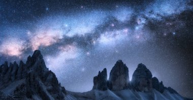 Samanyolu, yazın geceleri dağ tepelerinin üzerinde kemer görevi görür. Kemerli samanyolu ve parlak yıldızlı, yüksek kayalıklı mavi gökyüzü ile güzel bir manzara. Dolomites, İtalya 'da Tre Cime. Uzay ve galaksi. Seyahat