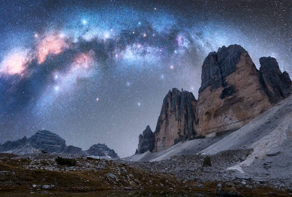 Milky Way arch over mountain peaks at night in summer. Beautiful landscape with blue sky with arched milky way and bright stars, high rocks. Tre Cime in Dolomites, Italy. Space and galaxy. Travel