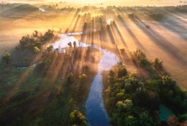 Ukrayna 'da sonbaharda güneşin doğuşunda sisli güzel kıvrımlı nehrin hava manzarası. Nehir kenarları, çayırlar, turuncu çimenler, sisli ağaçlar, sonbaharda şafak vakti altın güneş ışınları. Renkli hava manzarası. Üst görünüm
