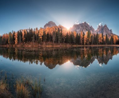 Sonbaharda gün doğumunda sudaki mükemmel yansıma ve portakal ağaçlarıyla birlikte. Dolomitler, İtalya sonbaharda. Kızıl ormanlı manzara, dağlar, göl, güneş ışınlı mavi gökyüzü. Renkli yapraklı ağaçlar