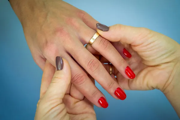 Nişan yüzüğüyle lezbiyen bir çiftin ellerini yakın plan çek. Kahverengi manikürlü bir kız başka bir kızın parmağına yüzük takıyor. mavi arka plan. yatay resim