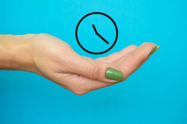 Zarif bir kadının eli nöbette. Yeşil manikürlü kızın elinde zamanın sembolü. mavi arka plan. yatay resim