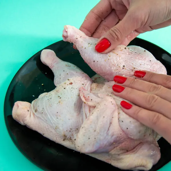 Tavuk pişirme süreci. Tavuk salamurası. Tavuk budu ovuyorum. Kuş siyah tabakta yatıyor. kare görüntü. kırmızı manikür