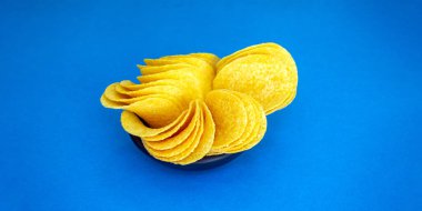 yuvarlak patates cipsi küçük siyah bir tabakta yatar. mavi arka plan. Kalori kaynağı. Atıştırmalık Bölgeye yerleştirme pankartı. Metin teleskobu alanı için yer. Yatay resim