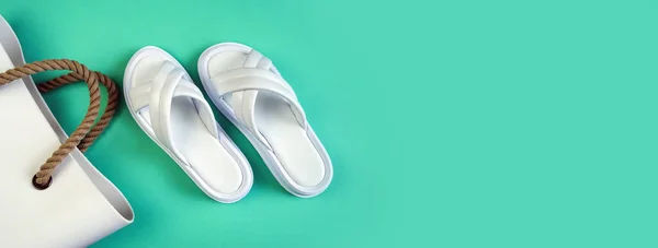 Women\'s summer white slippers and a white rubber bag with brown handles on a black background. Slippers. Banner for insertion into site. Place for text cope space. Horizontal image