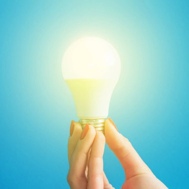Bir kadının elindeki lamba. LED lamba tutan kadın parmakları. Bir fikrim var. Yeni fikir ya da ilham konsepti. Başlangıç konsepti. mavi arka plan. Kare resim.
