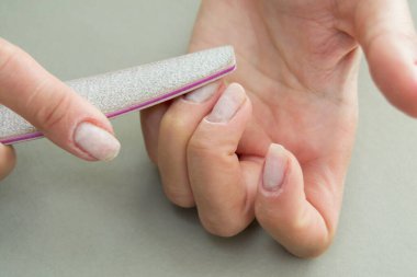 Çivi törpüleme işlemi. Beyaz verniği kesiyorum. Kadın manikürü, yakın çekim. Yatay resim.