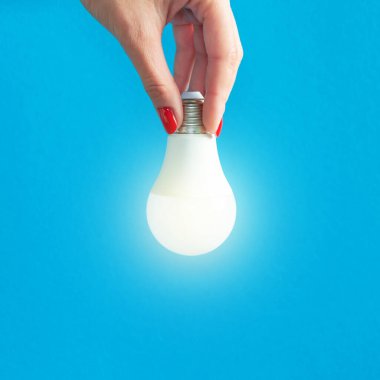 Bir kadının elindeki lamba. LED lamba tutan kadın parmakları. Bir fikrim var. Yeni fikir ya da ilham konsepti. Başlangıç konsepti. mavi arka plan. Kare resim.