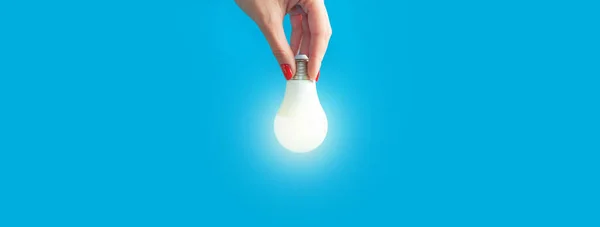 lamp in a woman\'s hand. female fingers holding LED lamp. idea. New idea or inspiration concept. Concept of startup. blue background. Banner for insertion into site. Place for text cope space.