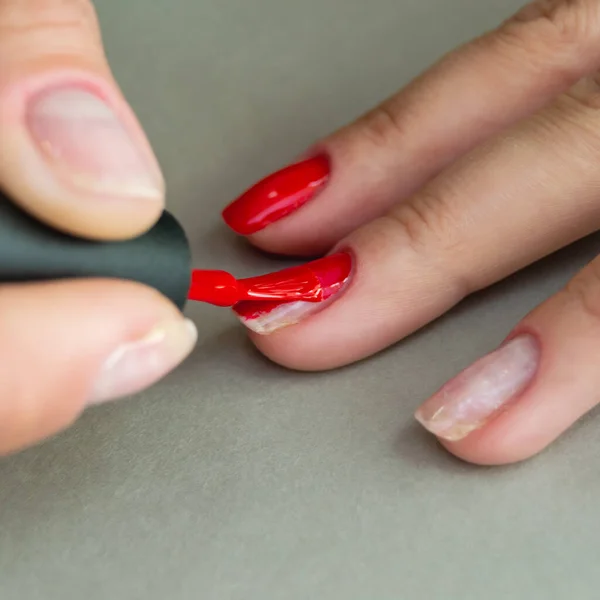 application of red gel polish on the nails of a woman\'s hand. part of the nails without coating. manicure at home. Square image.