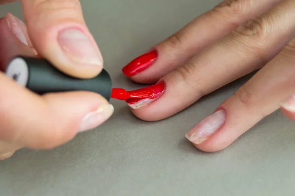 application of red gel polish on the nails of a woman\'s hand. part of the nails without coating. manicure at home. Horizontal image.