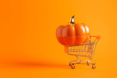 Turuncu arka planda büyük balkabağı ve fotokopi alanı olan oyuncak alışveriş arabası. Cadılar Bayramı afişi, alışveriş konsepti. Satış fikri..