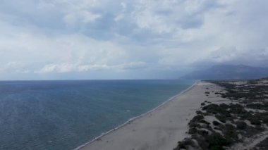 Uzun kumlu bir sahil yüksekliğinden drone görüntüsü, deniz, bulutlar, kumlu dağlar