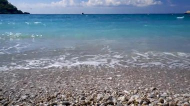 Turkuaz deniz, mavi gökyüzü, beyaz köpük ve çakıl taşı plajı yakın çekim
