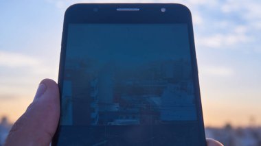 Elinde cep telefonuyla şehrin fotoğraflarını çekiyor.