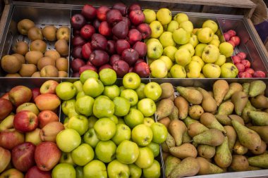 Bir markette çeşitli tipte yeşil ve kırmızı elma ve armutlar sergilenir..