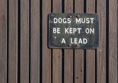 Ahşap bir duvarda siyah-beyaz metal tabela var. Köpekler kurşun geçirmez diyor..