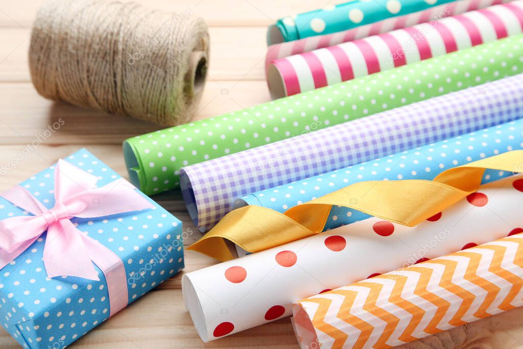 Rolls of craft papers with gift box and ribbon on wooden background